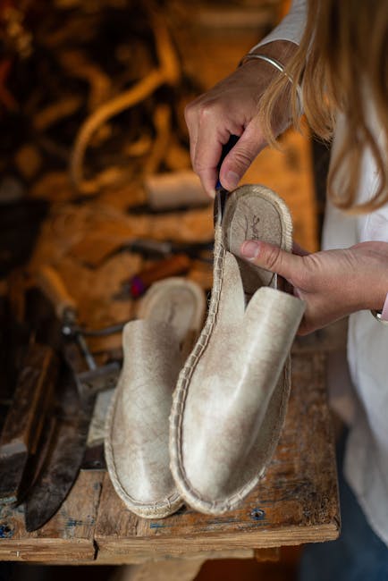 Close-up of artisan hands crafting leather shoes on a rustic wooden workbench.