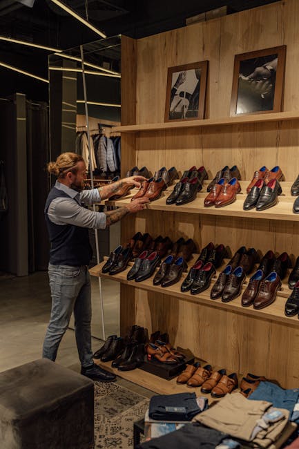 A man arranging luxury leather shoes on a wooden shelf in a stylish shoe store.